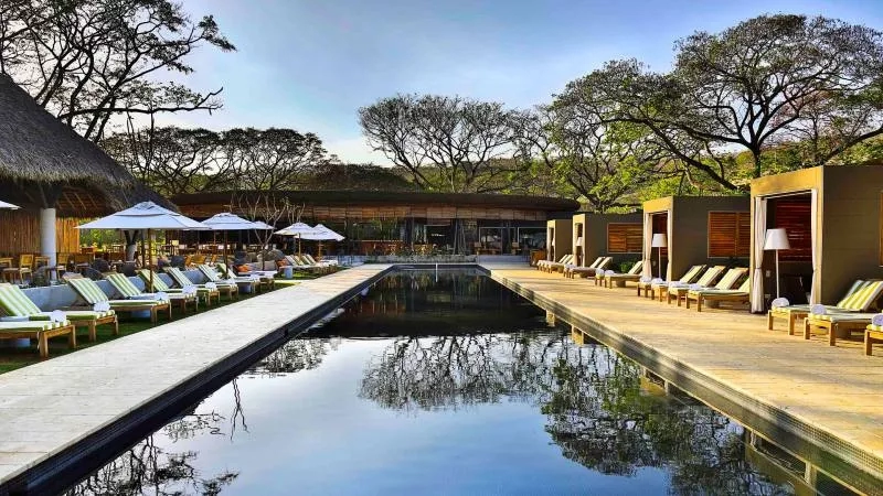 Outdoor pool with lounge chairs, umbrellas, and tropical architecture at a luxury resort.
