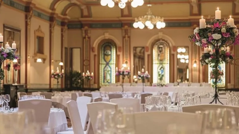 A wedding venue with white chairs, tables, chandeliers, candles, and flower arrangements.