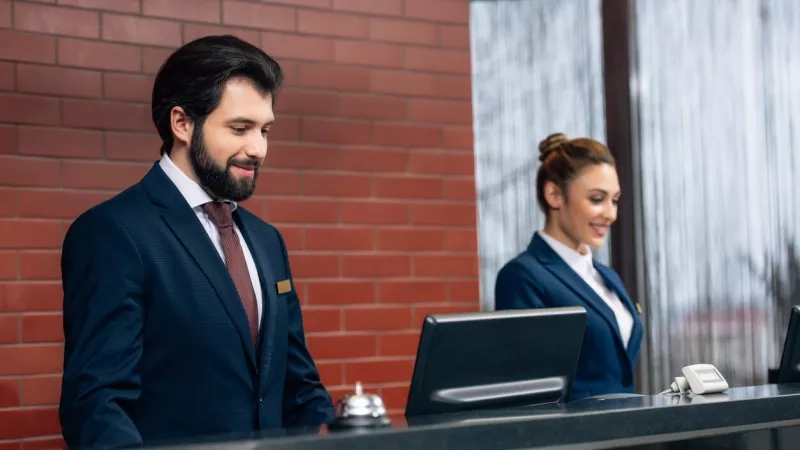 A smiling woman helps a man check in at the front desk of a hotel.