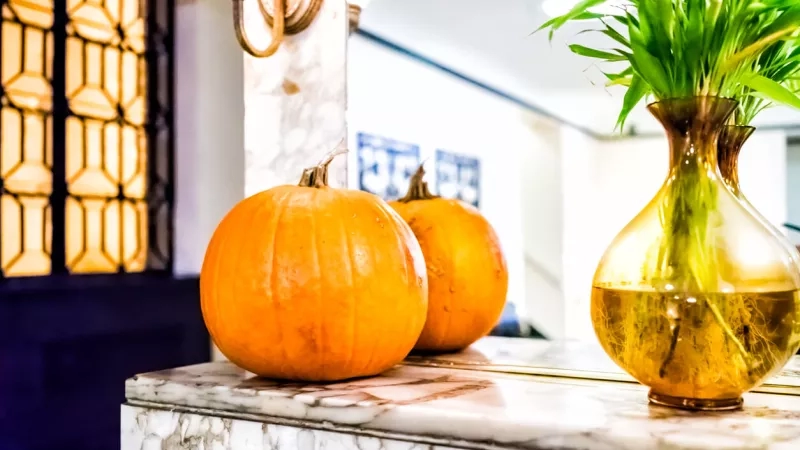 Pumpkins and a vase with plants are on a marble surface inside The Westin Excelsior, Rome.