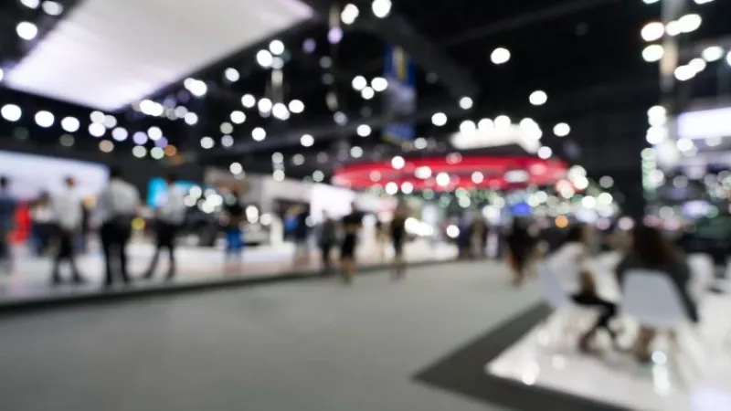 Blurry image of people walking around a large room, probably at a trade show event.