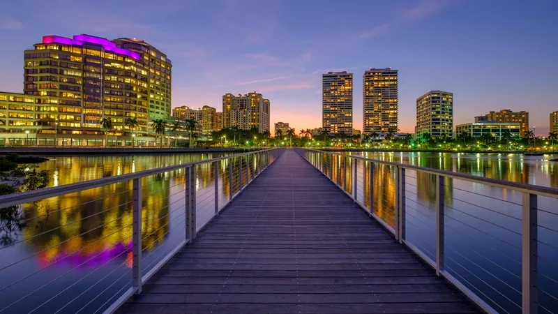A cityscape of a modern city, featuring a wooden walkway over a serene body of water.