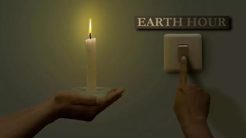 A candle is lit in a person's hand, and a power switch is off during Earth Hour.