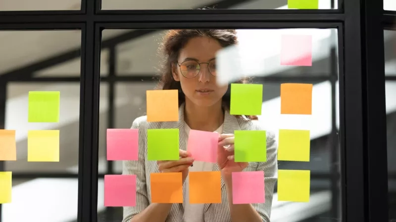 Woman in office with post-it notes on window for project management with Kanban.