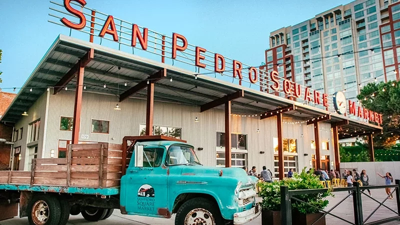 Blue vintage truck parked in front of the San Pedro Square Market with a tall building behind it.