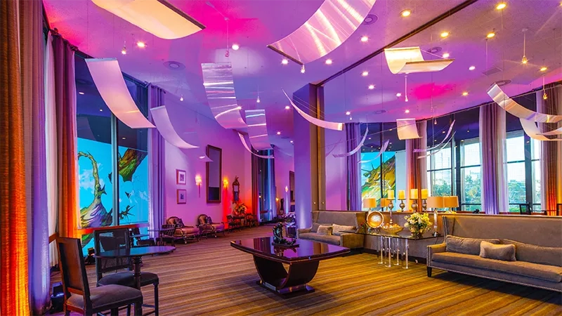 A picture of a lobby with couches, tables, and chairs, with a purple and pink lighting ambiance.