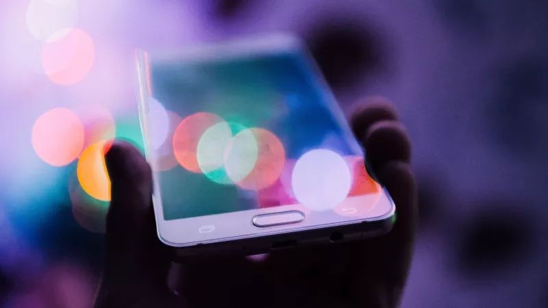 Close up of hand holding a smartphone with a blurred background of colorful bokeh lights.