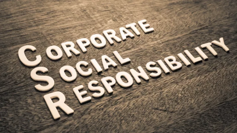 Wooden surface with white letters spelling out "Corporate Social Responsibility" on a rustic, grainy background.