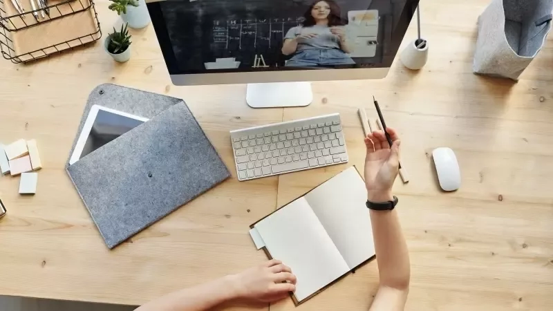 Person sketching on a notebook while watching a presentation on a computer screen during a virtual event.