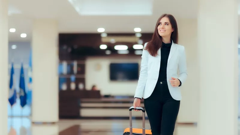 Female executive hotel guest walking through lobby wheeling suitcase at the Hotel RL by Red Lion.