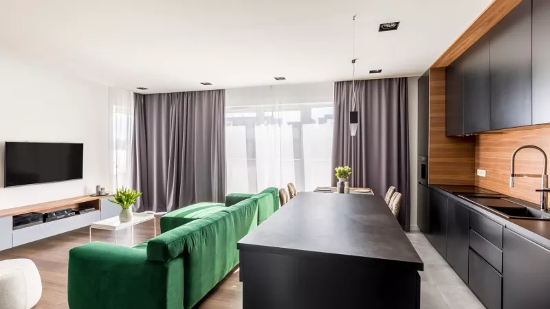 Modern apartment kitchen with island, dining area, and living room with sofa and TV on the wall.