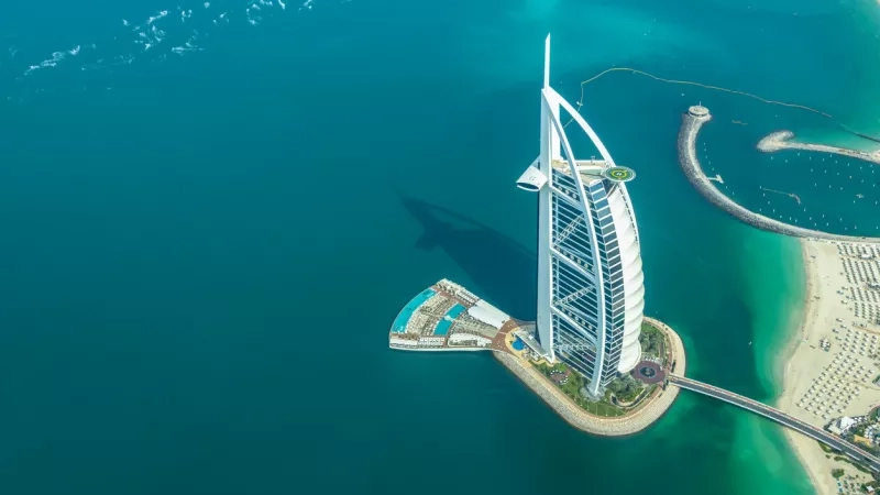 Aerial view of Burj Al Arab luxury hotel in Dubai with green waters and blue sky.