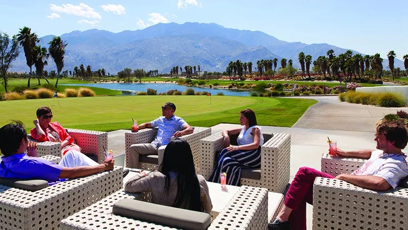 People sitting on outdoor lounge chairs overlooking a golf course at the Omni Rancho Las Palmas Resort.