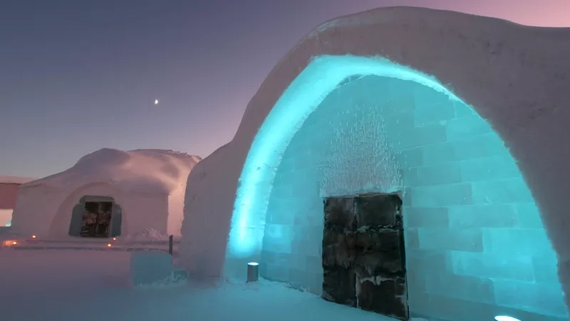 Entrance to an ice hotel in Sweden with blue lights and a moon in the background.