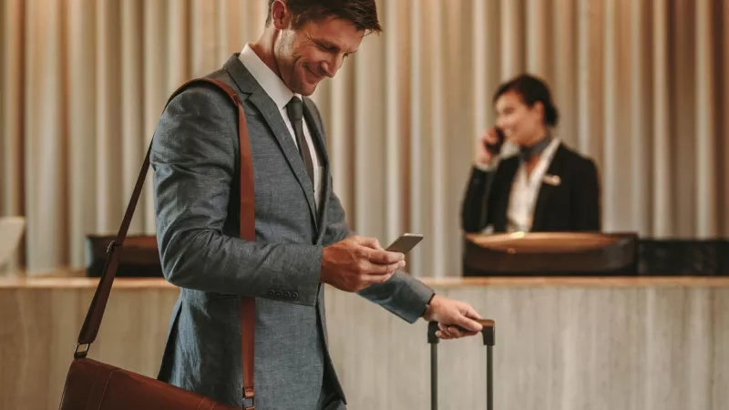 Hotel guest smiling looking at mobile device as he checks in at the front desk.
