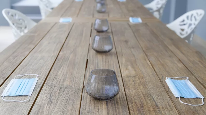 Glasses and masks on a wooden table outside with chairs in the background.