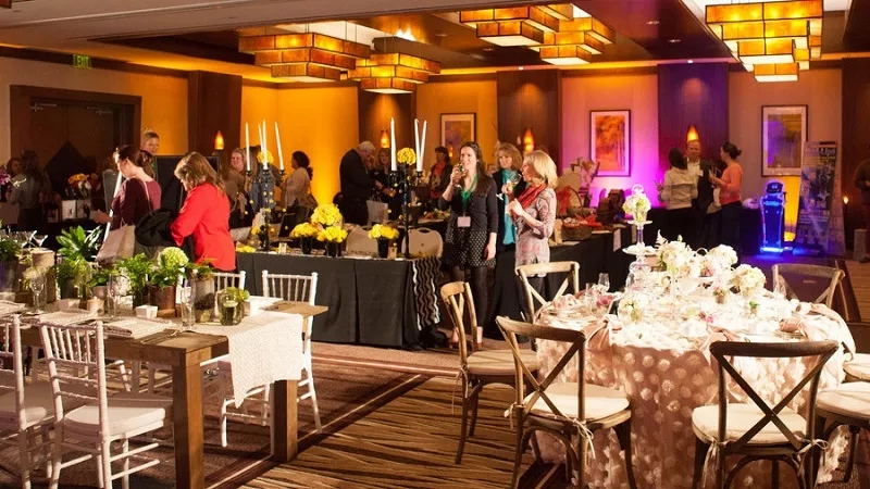 People gather at a banquet hall with large tables, candles, and flowers for a special event.