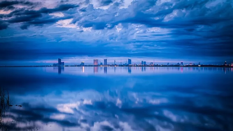 A city skyline with reflections in the water during the blue hour with clouds in the sky.