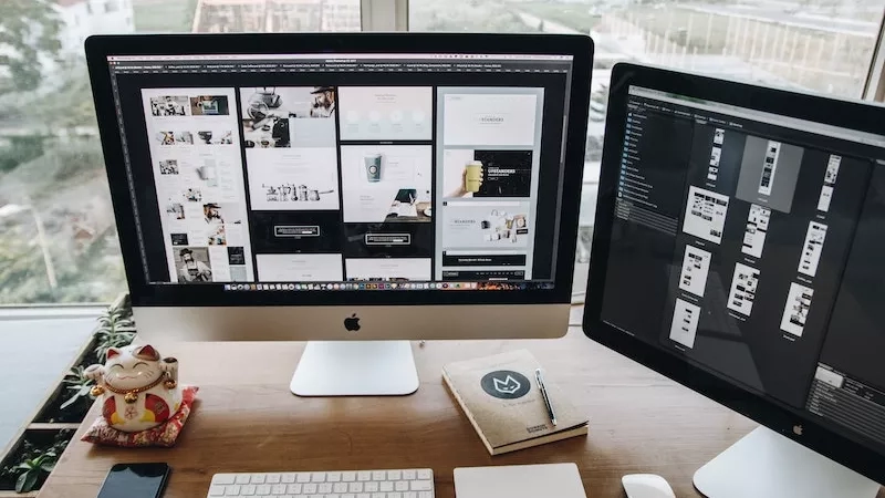 Virtual marketing: two computer screens with keyboards and mice on a desk in front of a window.
