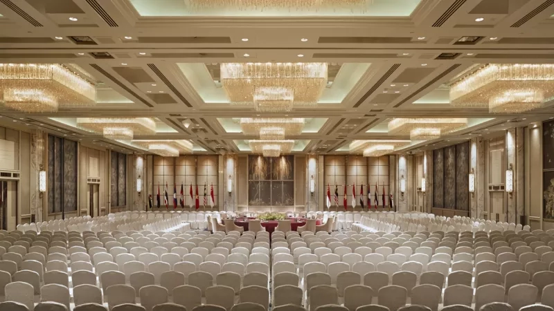 A large conference room with white chairs and flags in the center at The St. Regis Beijing.