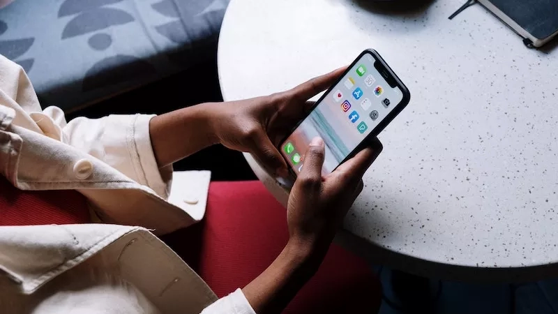 Woman in cafe using phone with apps like Instagram and TikTok on the screen.