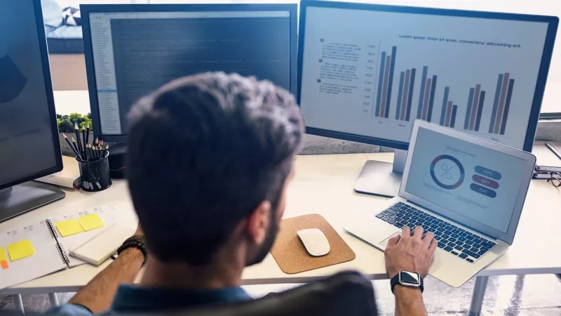 Man tracking competition data on computers at office, showing the importance of market research.
