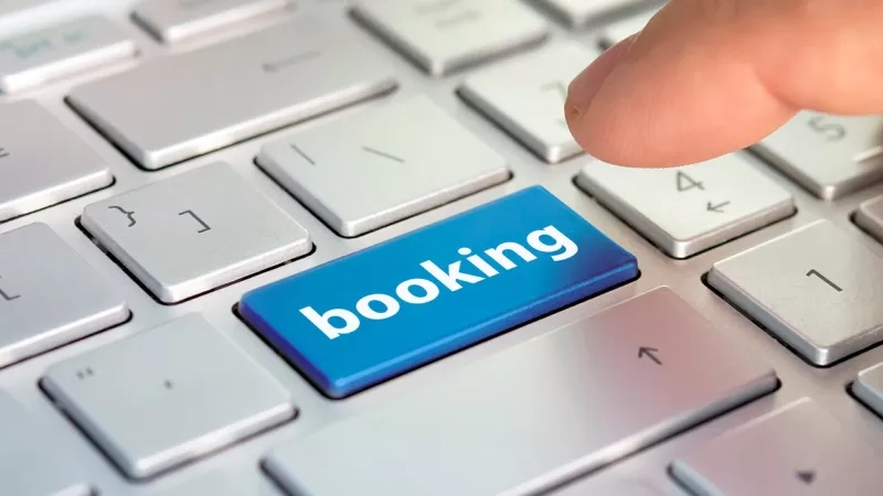 A person's finger pressing a blue booking button on a computer keyboard to book a hotel.
