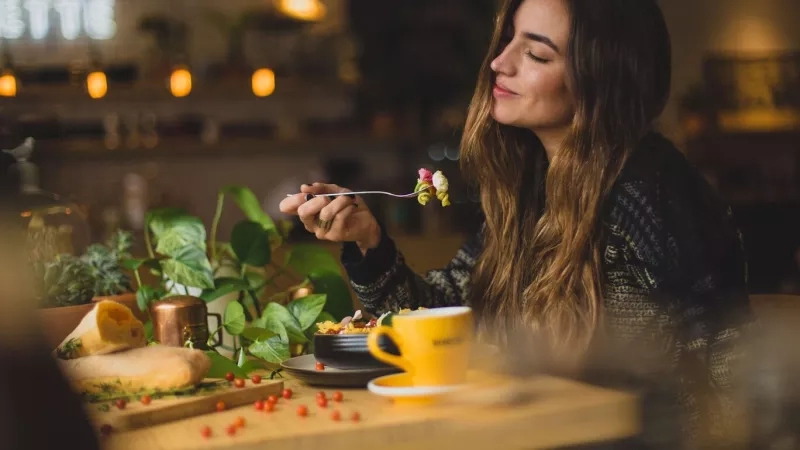 Woman eating salad at a table with plants and a yellow mug at a restaurant called Pette.