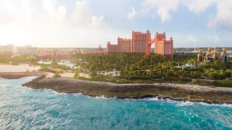An aerial view of Atlantis resort, with ocean waves, lush trees, and a clear sky.