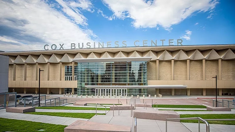 Cox Business Center with modern architecture, glass entrance, and well-maintained landscaping under a blue sky.