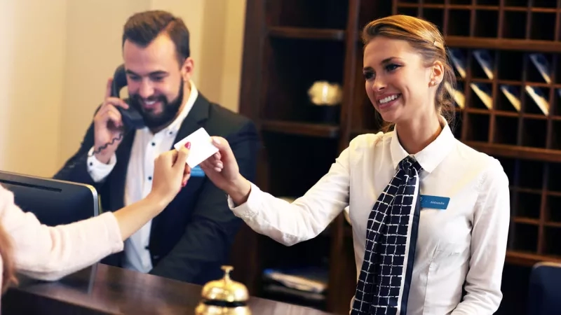 Smiling hotel employee leaving positive first impression on guests at the front desk of the hotel.
