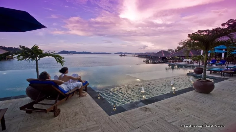 A couple enjoying the sunset from a resort pool with ocean view.