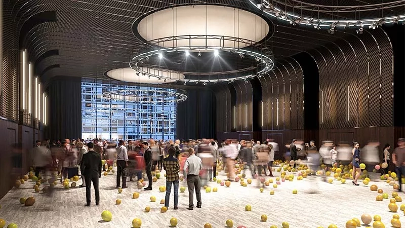 People walking around the room filled with yellow balls and pink balls, with a glass wall in the background.