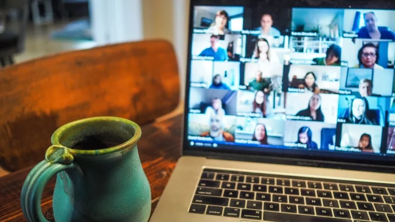 Laptop on a table with a cup of coffee and a virtual meeting displayed on the screen.