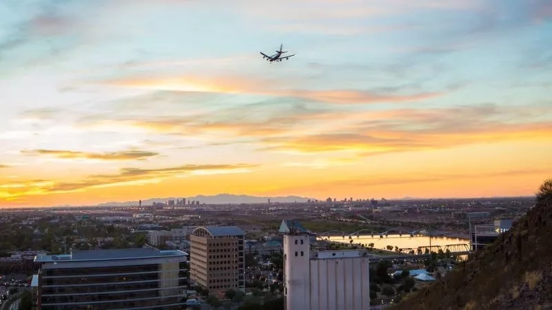 British Airways Tempe in Arizona, featuring an airplane in the sky during sunset, with buildings and a river.