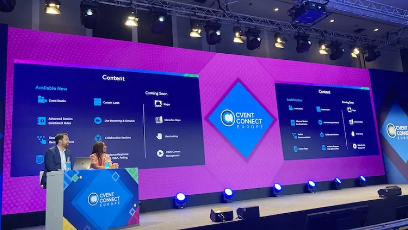 A man speaks on a stage with a woman and a screen with the words "Event Connect Europe".