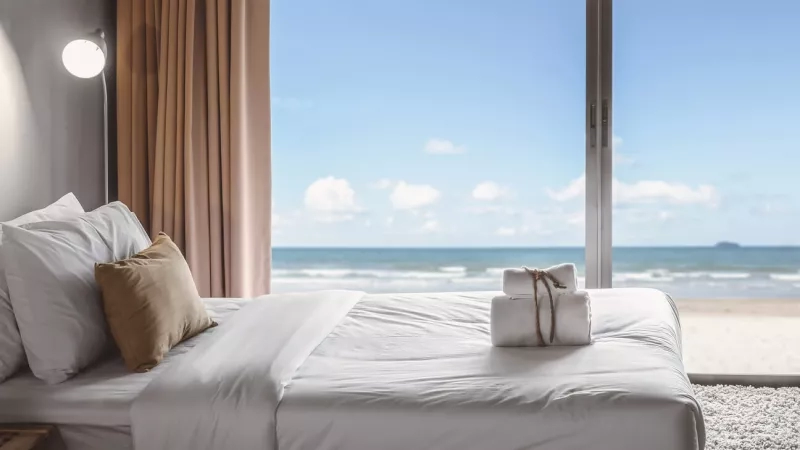 Hotel room with a bed, white towels, and a window overlooking the beach and ocean.
