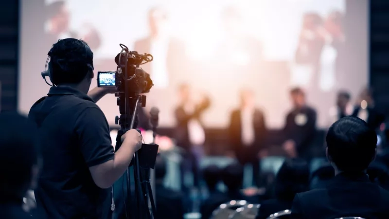 A person is capturing the video of an event in a conference hall with a camera.