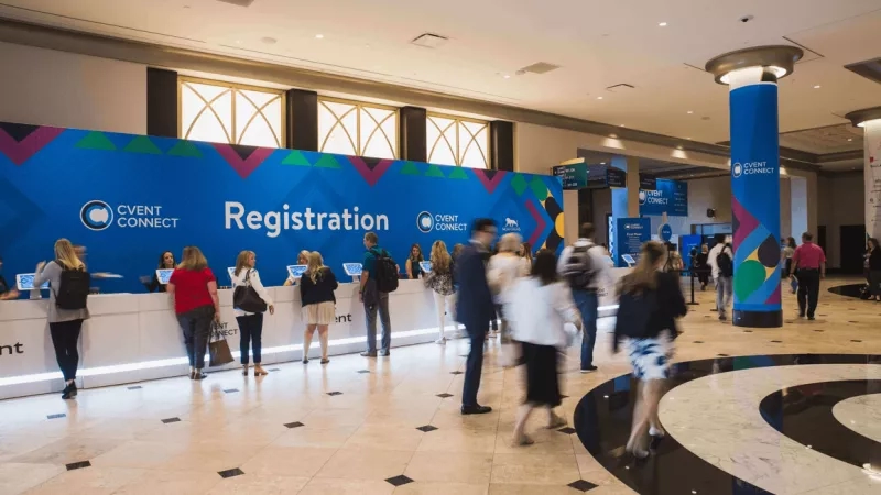 Several people standing at the registration desk of Cvent Connect, with blue and purple decorations around the area.