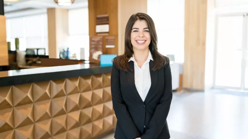 Hotel general manager smiling in lobby at the front desk of a hotel.