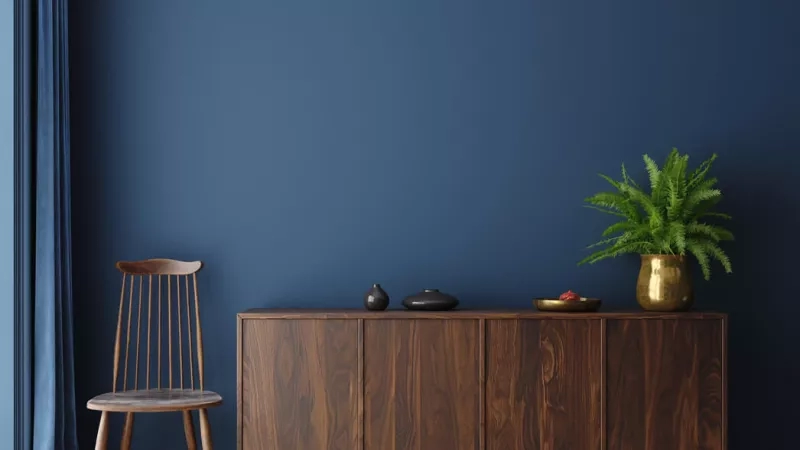 Wooden cabinet with a plant on top in a room with blue walls and wooden floors.