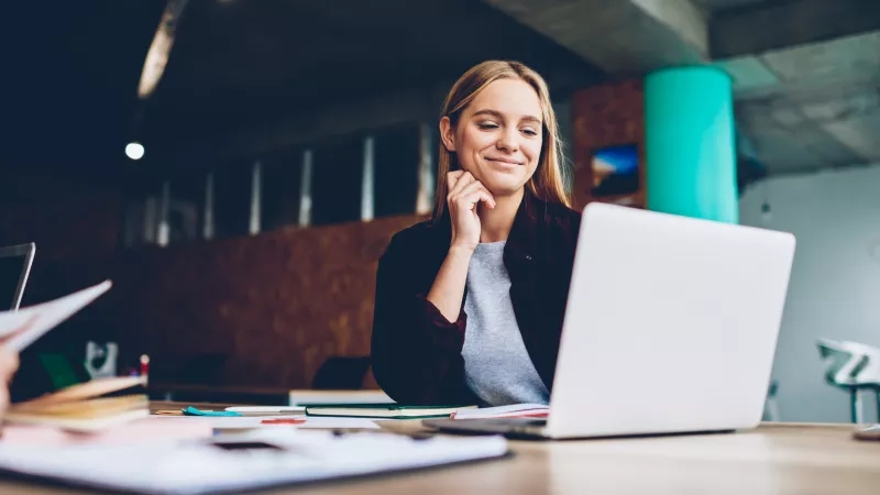 A woman is working on a laptop in a modern office with a bright and airy ambiance.