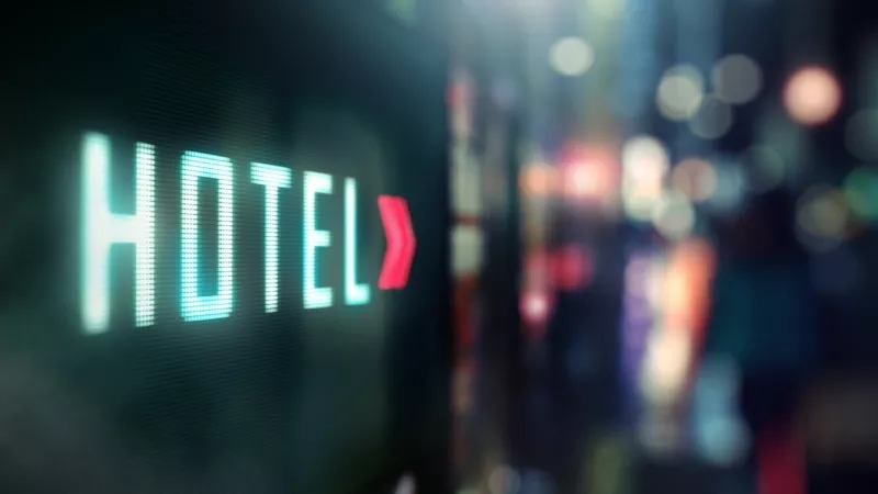 Close-up shot of LED hotel digital signage, glowing in the night, with a blurred city in the background.