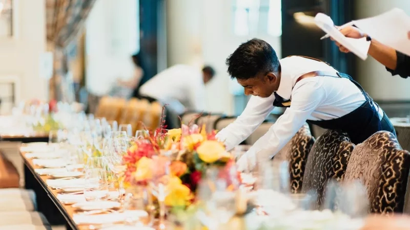 A waiter in formal attire is setting a table at a restaurant, creating a refined atmosphere.