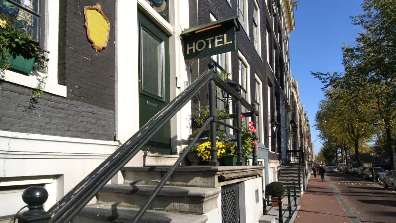 Exterior view of the entrance of the small hotel, with stairs, railings, and a green board with the text "Hotel".