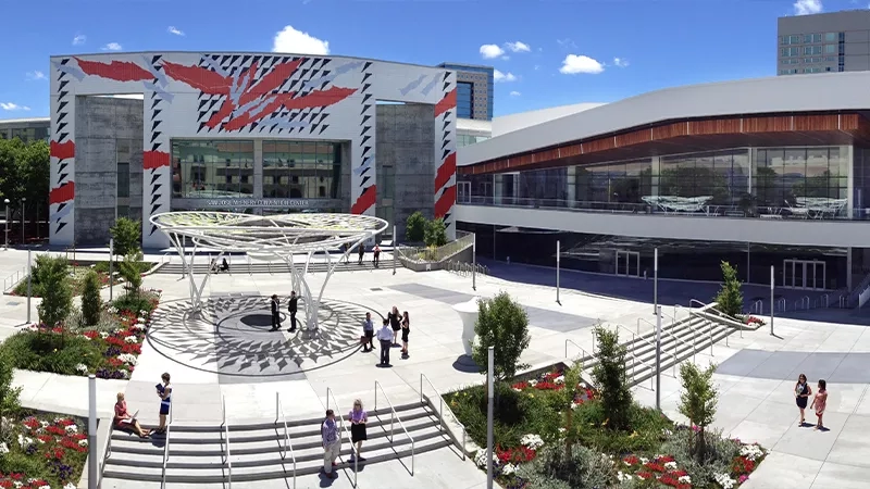 Exterior view of the San Jose McEnery Convention Center with people, architecture, landscaping, and a clear sky.