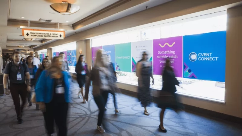 Several people are walking down a hallway with a large Cvent Connect banner on the wall.