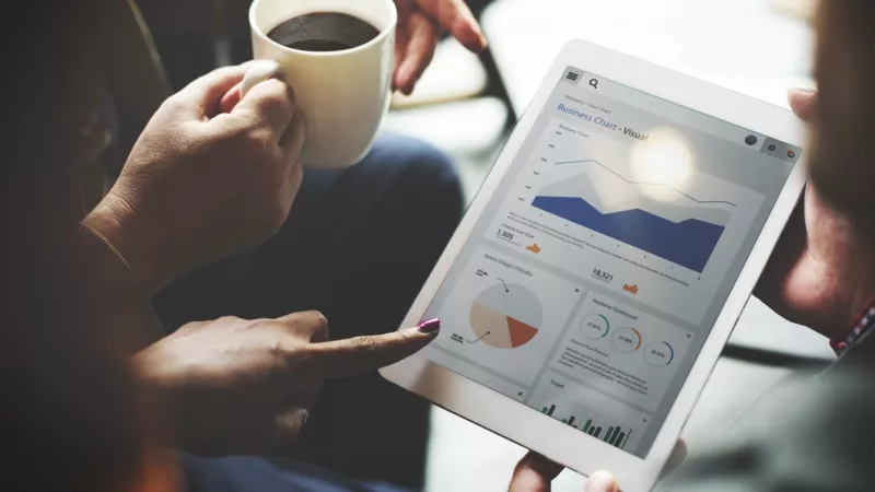 Two people holding a tablet with a business chart visual while pointing at a specific data.