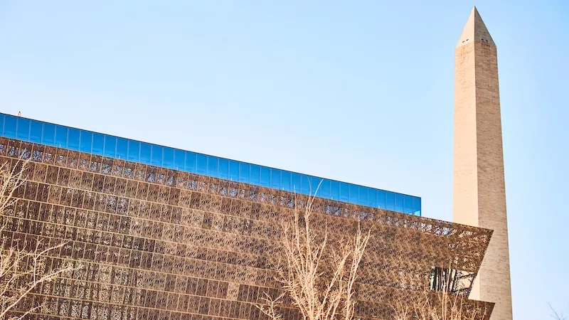 Exterior of the Smithsonian National Museum of African American History and Culture with the Washington Monument in the background.