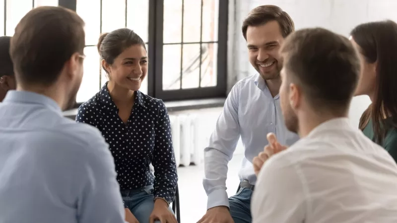 Group of people sitting smiling during team-building activity at the office.